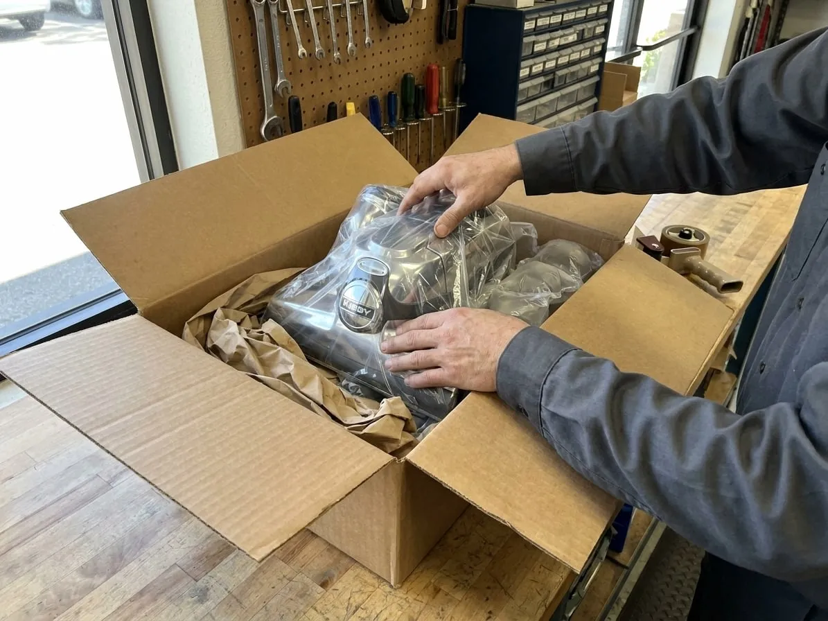 Technician packing a Kirby vacuum wrapped in plastic into a padded shipping box