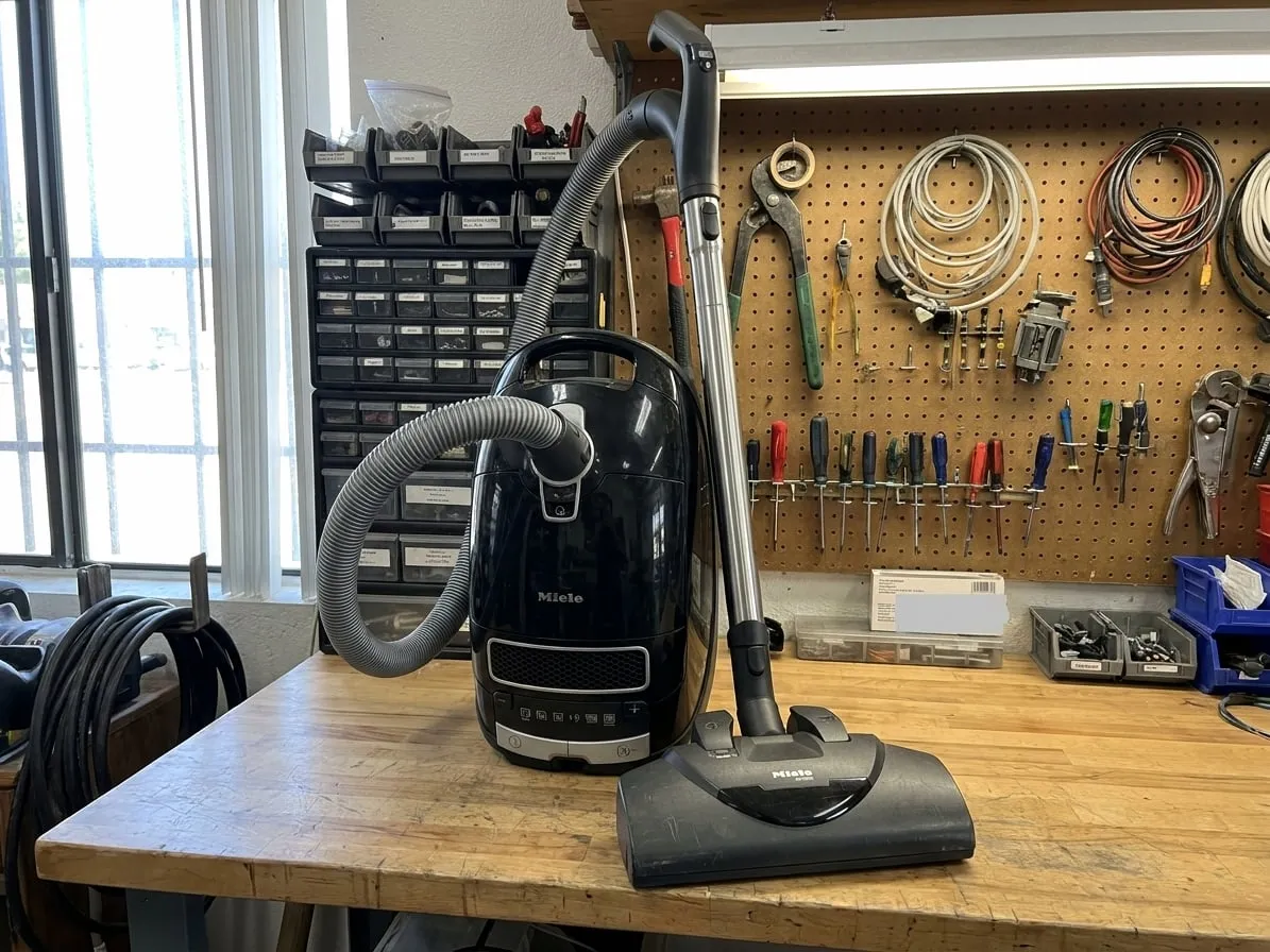 Black Miele Complete C3 canister vacuum with its hose, wand and electric power brush on a workbench