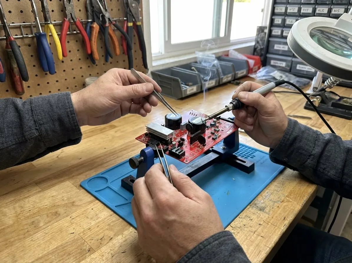 Technician soldering a component on a red Rainbow vacuum control board held in a PCB vise