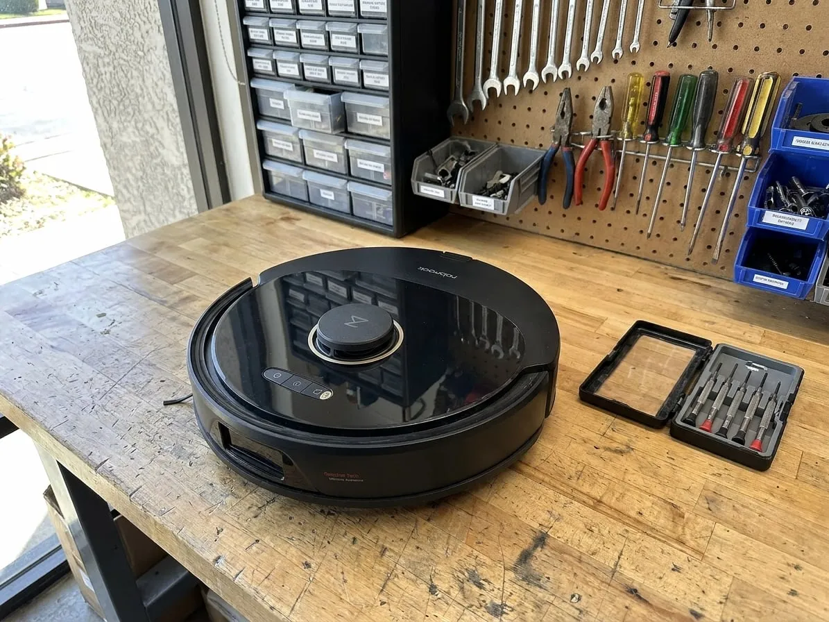 Black robot vacuum with a LiDAR turret on a workbench, without its dock